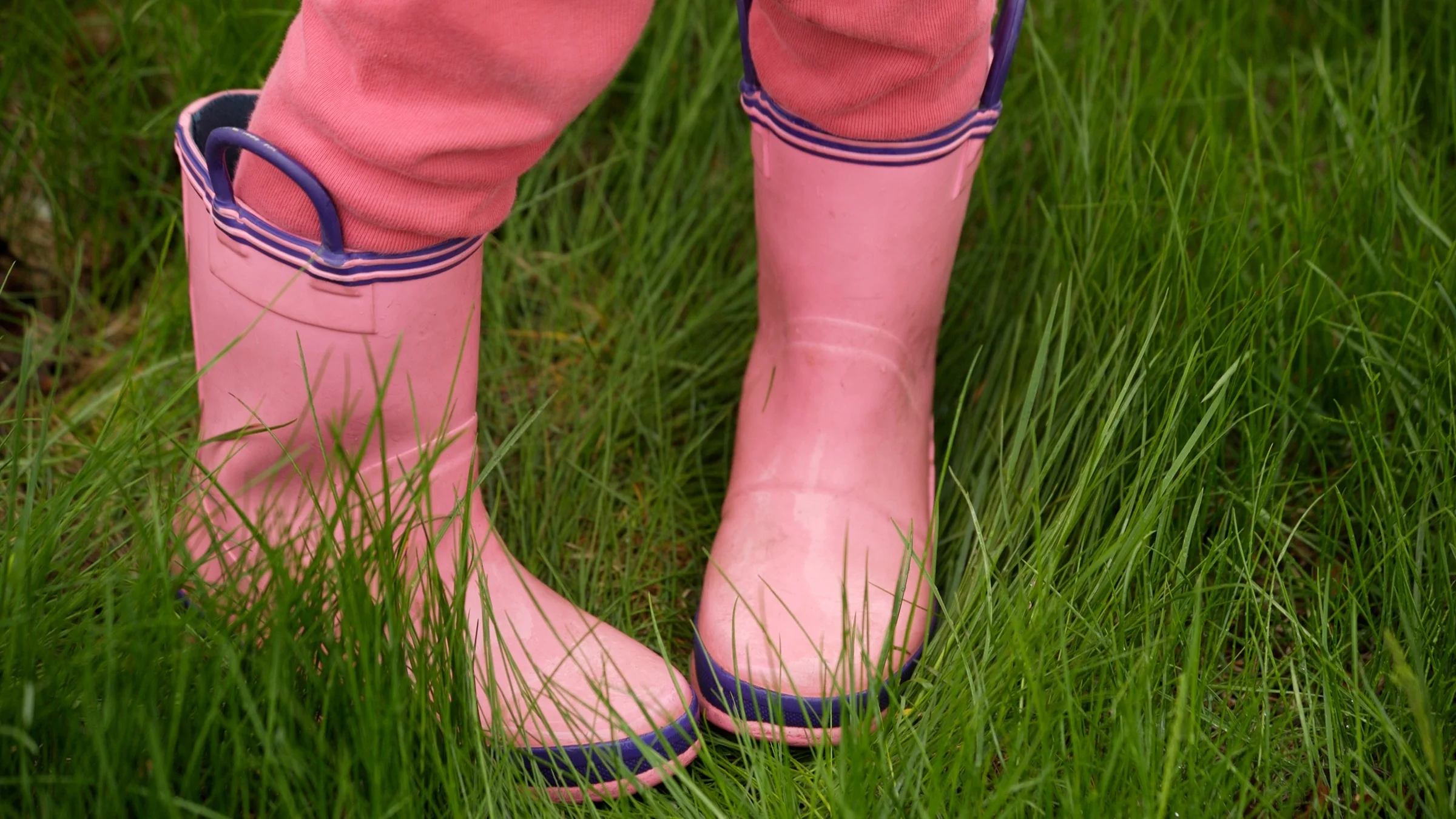 A close-up image shows a young child in rain boots with their toes pointed in toward each other.