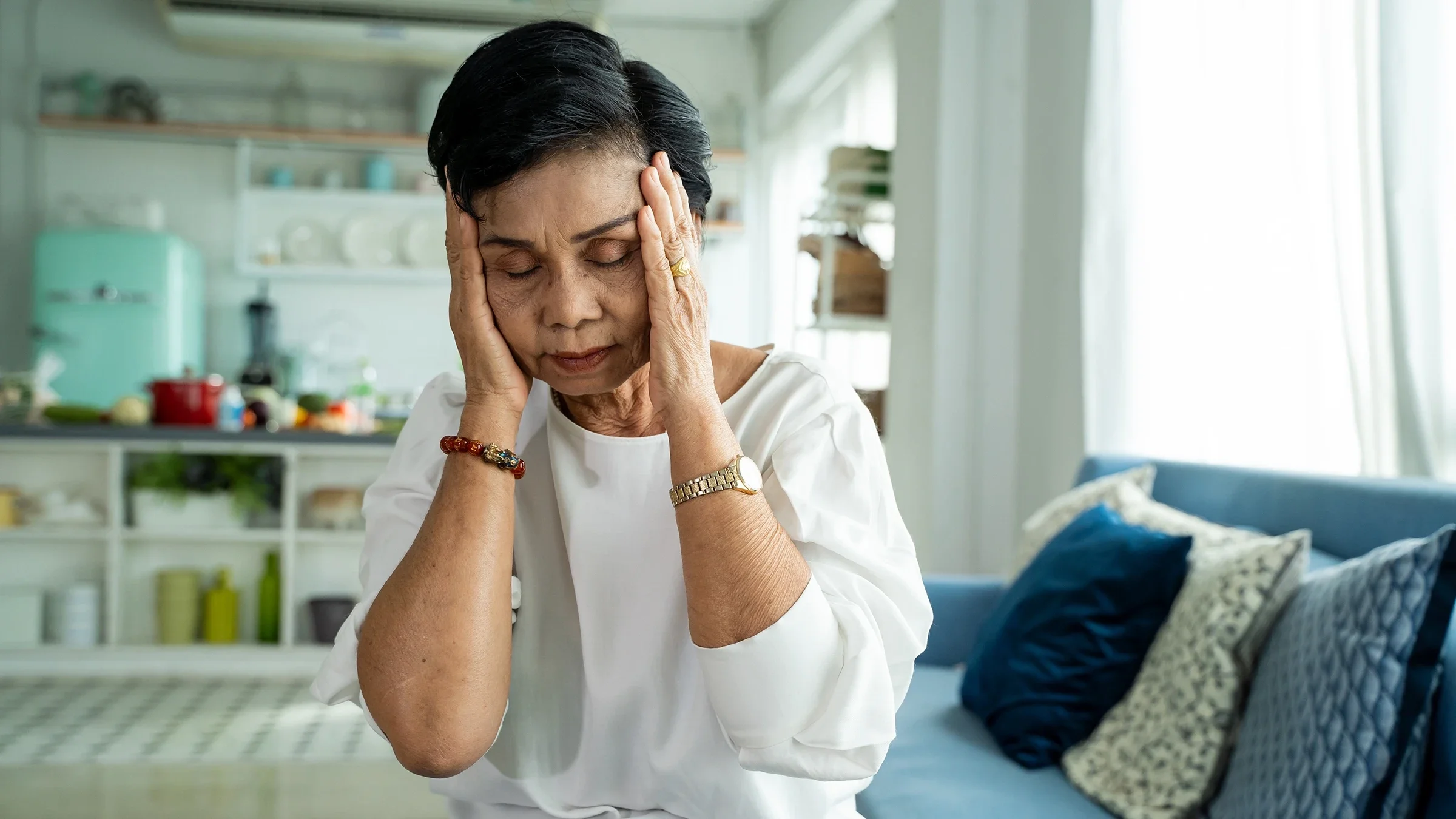 Senior woman holding her temples and closing her eyes. She is suffering from a severe headache.