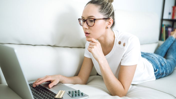 A person on their couch, looking up medications on their laptop.