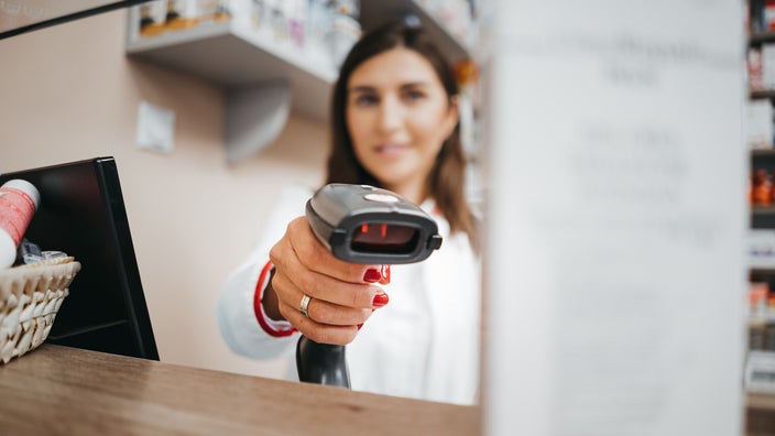 A pharmacist is scanning a medication box with a price scanner. 