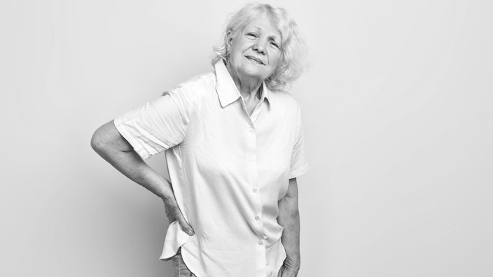 Black and white portrait of an elderly woman with her hand on her back.