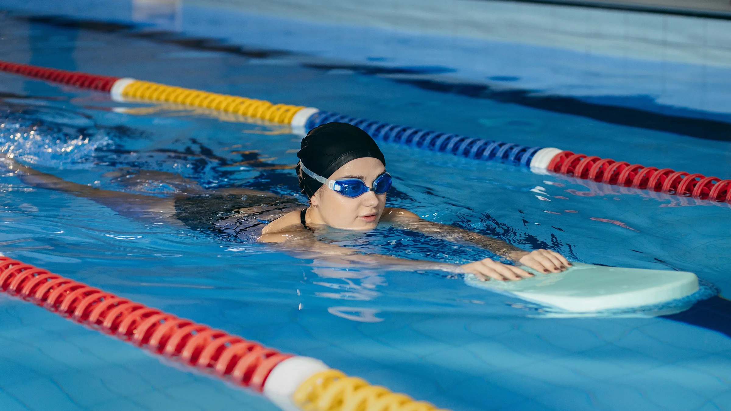 A young woman is wearing goggles while swimming with a board in the pool.