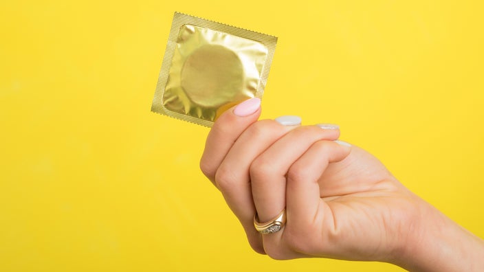 Hand holding a condom on a yellow background.