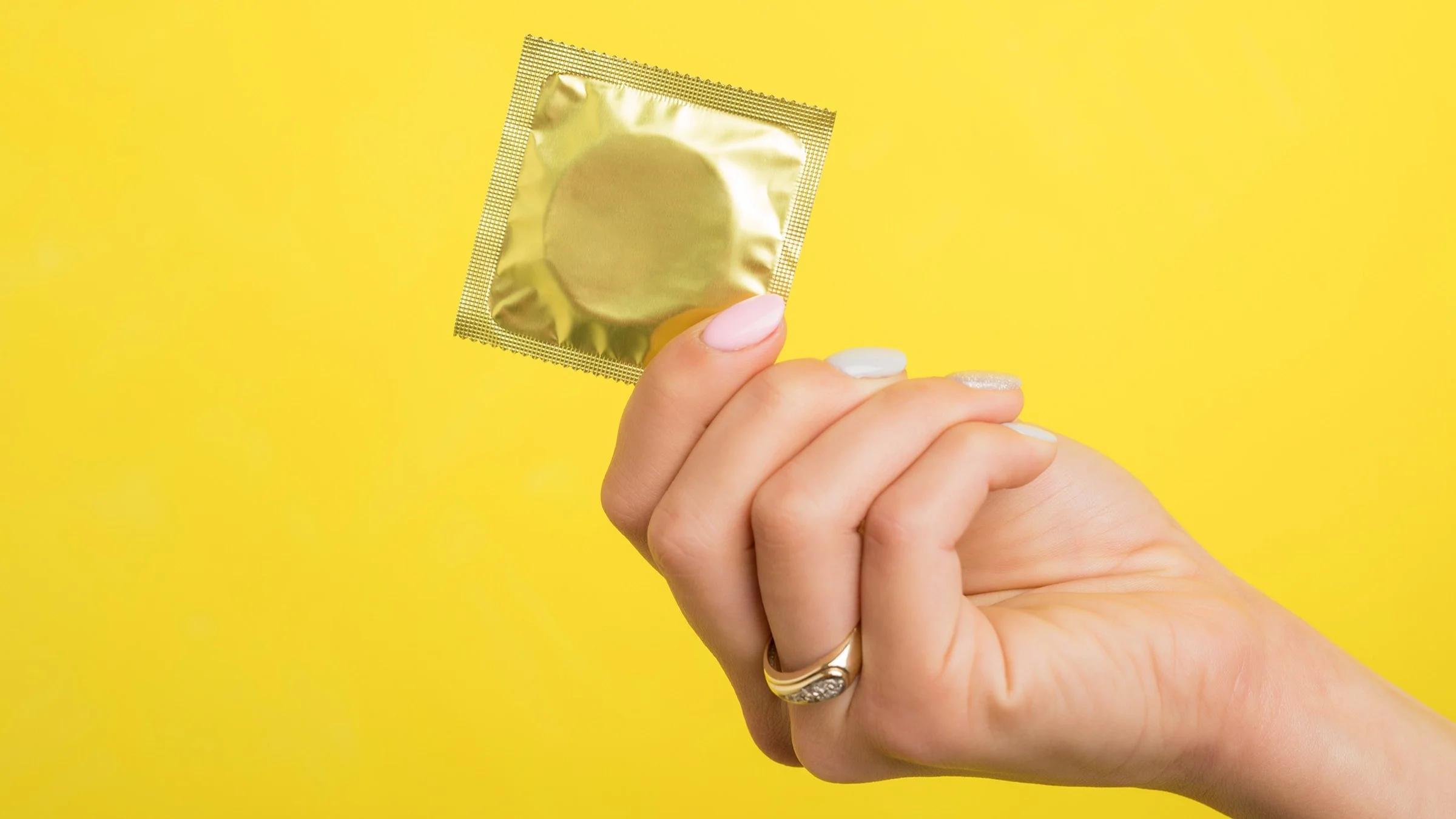 Hand holding a condom on a yellow background.