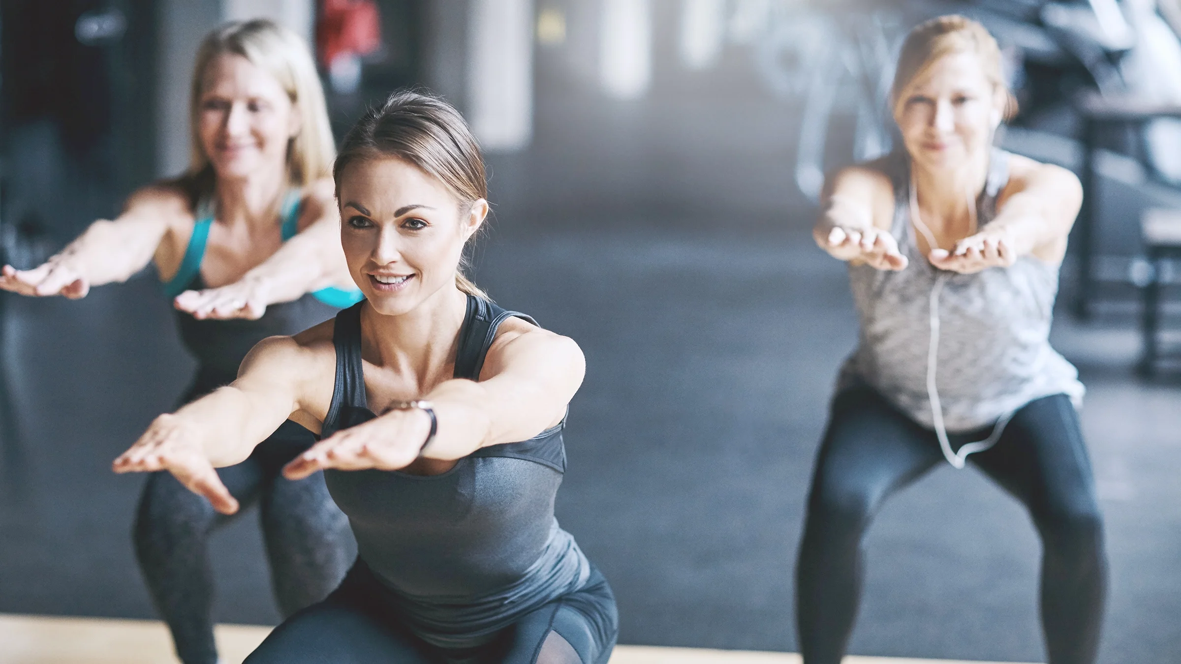 Three women at a HIIT workout class. They are doing squats. 