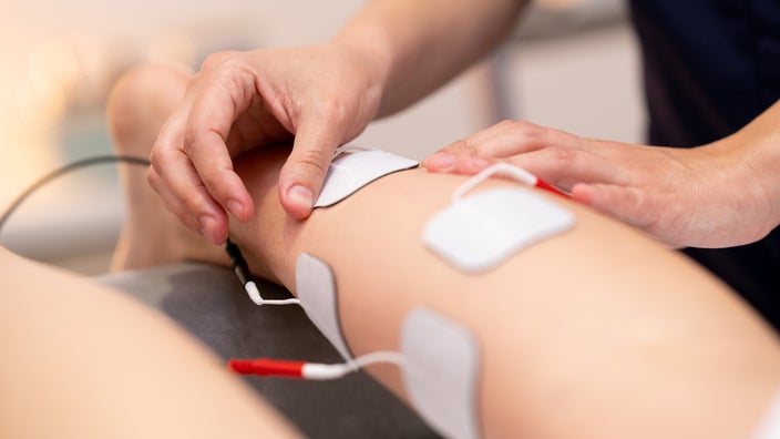 A healthcare professional places electrodes on a person’s leg. 