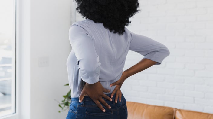 A woman holds her lower back. People who have a bruised tailbone can experience pain while sitting, standing, or bending over.