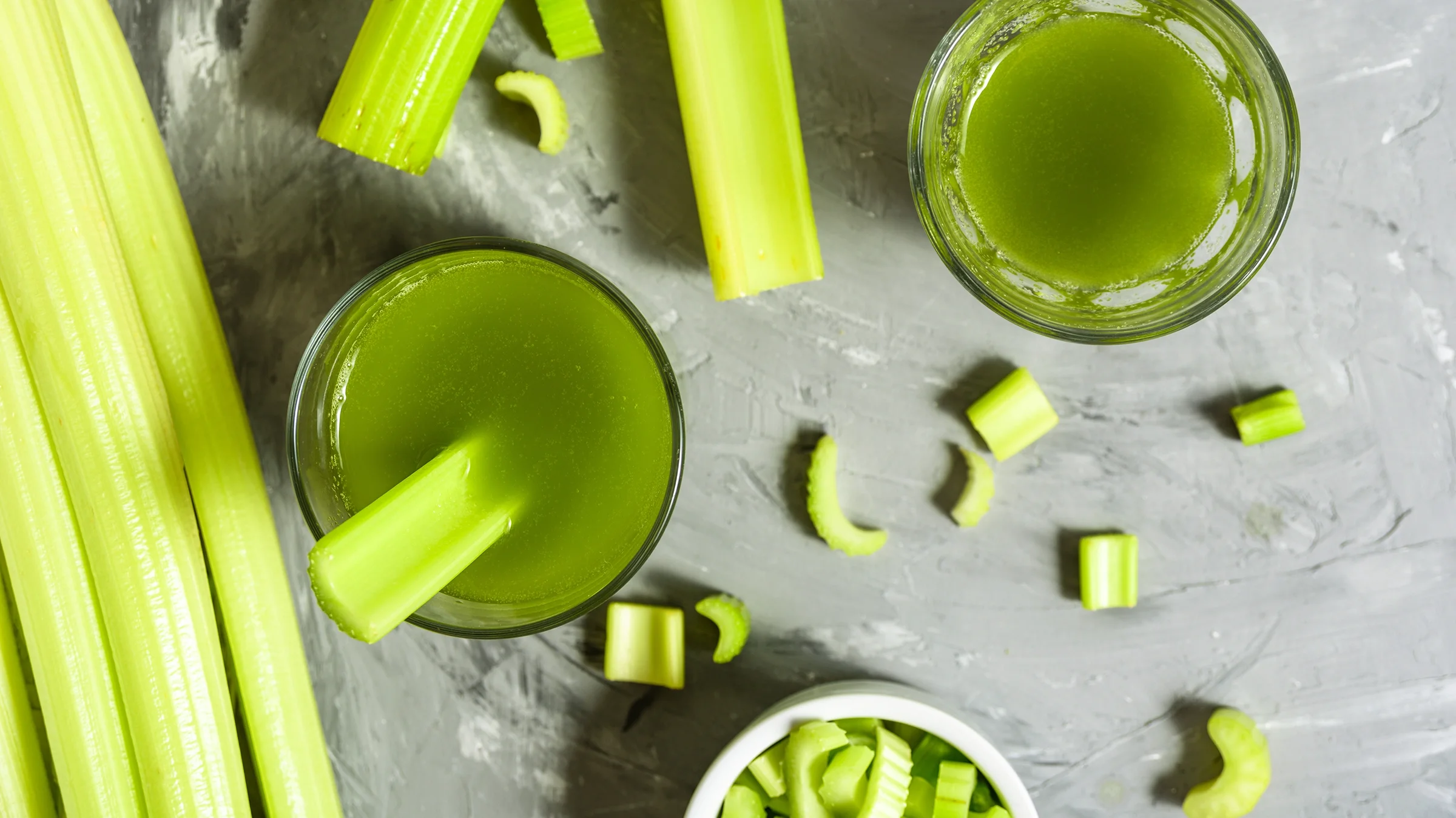 Overhead shot of celery juice in cups with celery stalks surrounding. There is added text on top reading “Health Debunked” with a yellow highlight bar behind it.