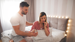 A woman sitting in bed taking a pill, being comforted by her partner.
Jelena Danilovic/iStock via Getty Images Plus 
