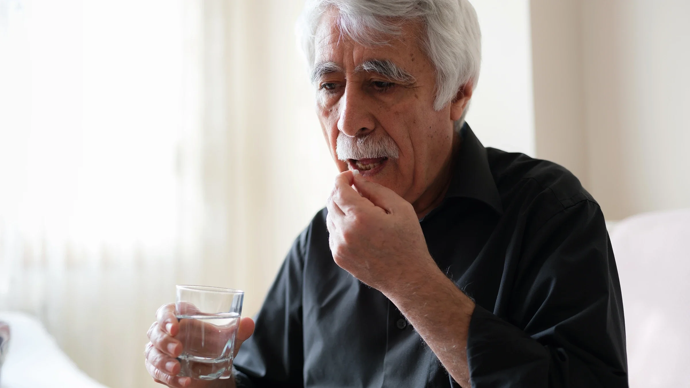 A man holding a glass of water prepares to take a pill.