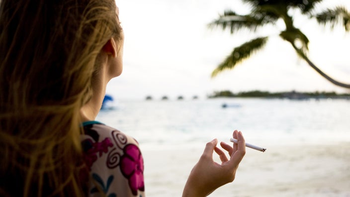 A woman smokes a cigarette on the beach. Smoking can affect the health of your skin and can cause premature skin aging.