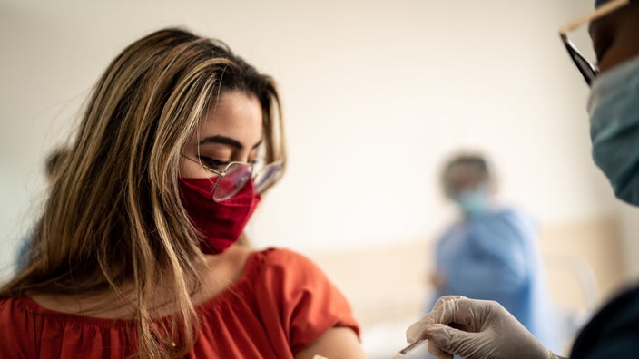 Young woman with glasses and red face mask getting the COVID-19 vaccine from a nurse.