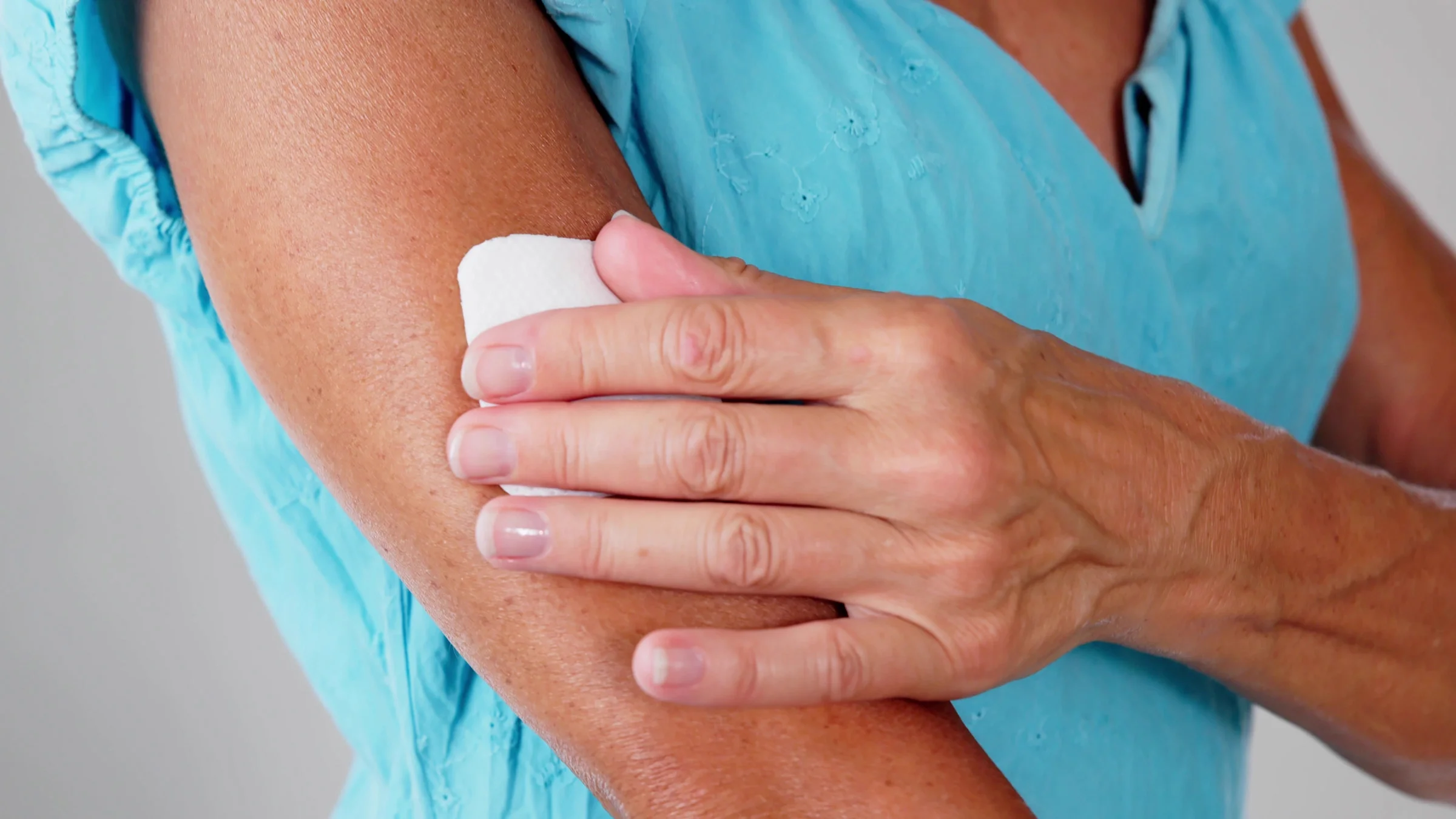 Close-up of someone sticking a medication patch on their arm.