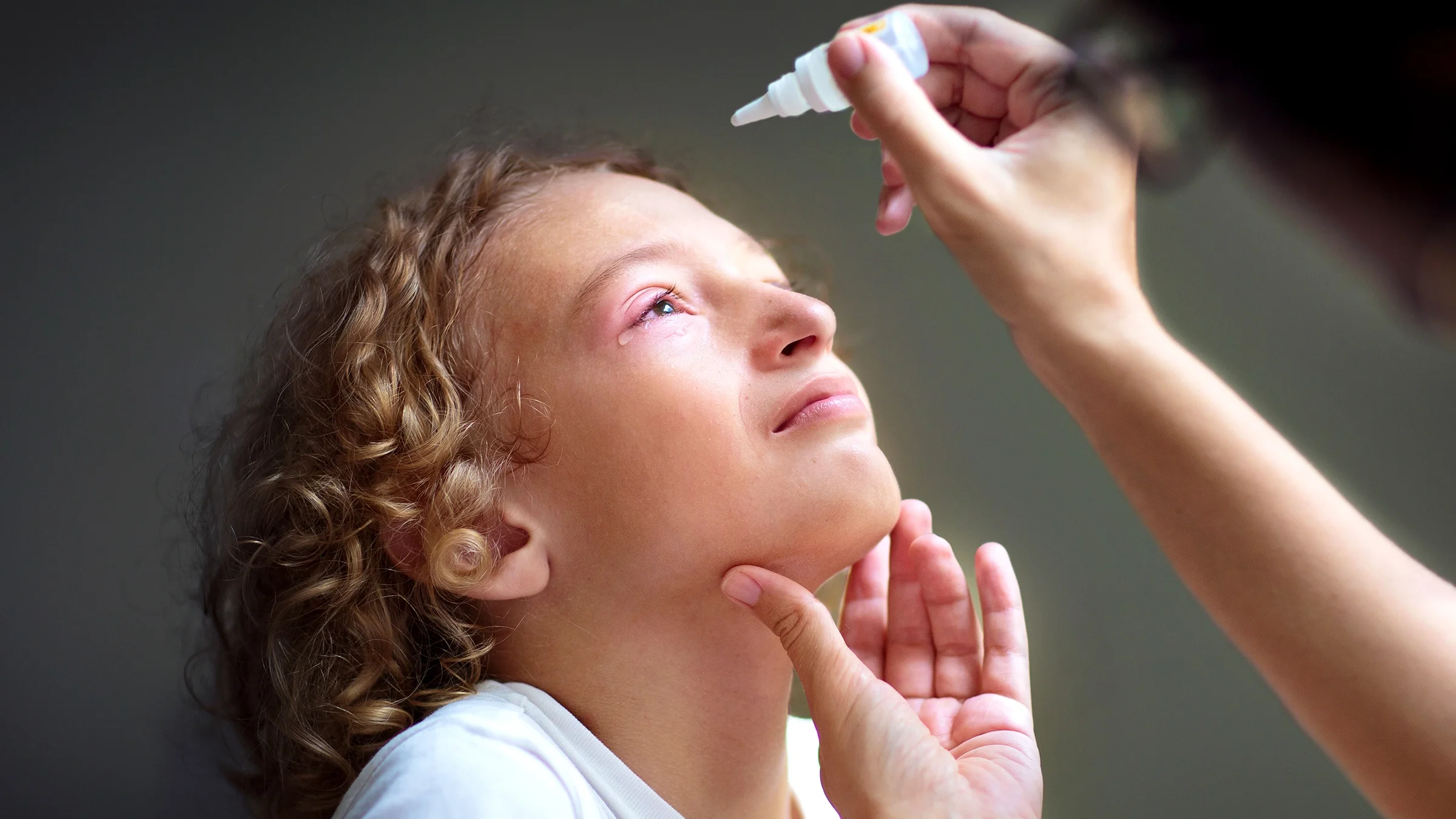 Child with pink eye receiving eye drops.