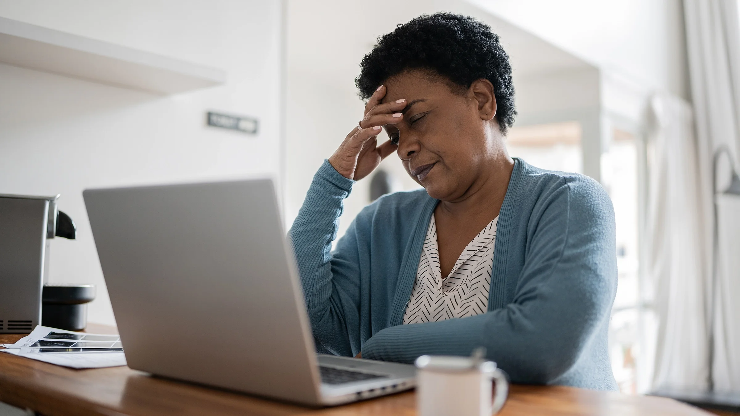 Woman with a headache sitting at her laptop at home.