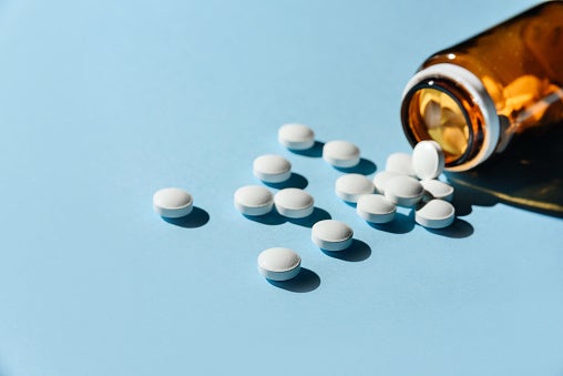 Glass pill bottled spilled onto light blue background with tablets scattered out.