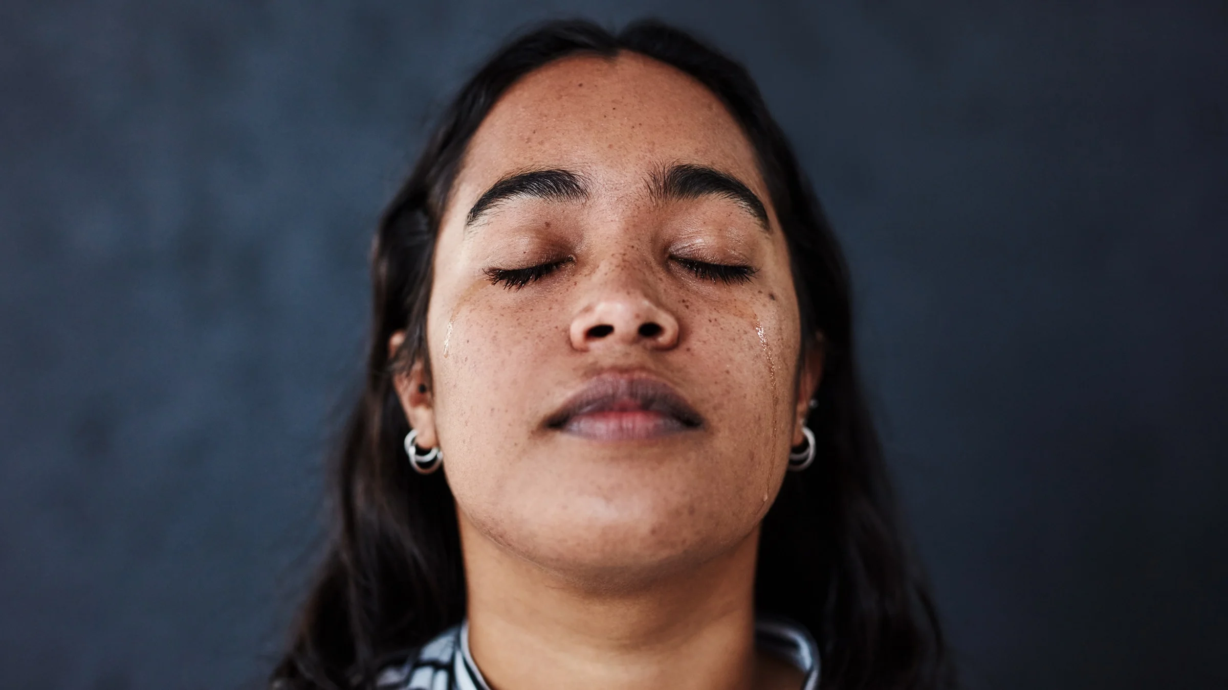 Close-up portrait of a young woman closing her eyes with a tear running down her cheek. 