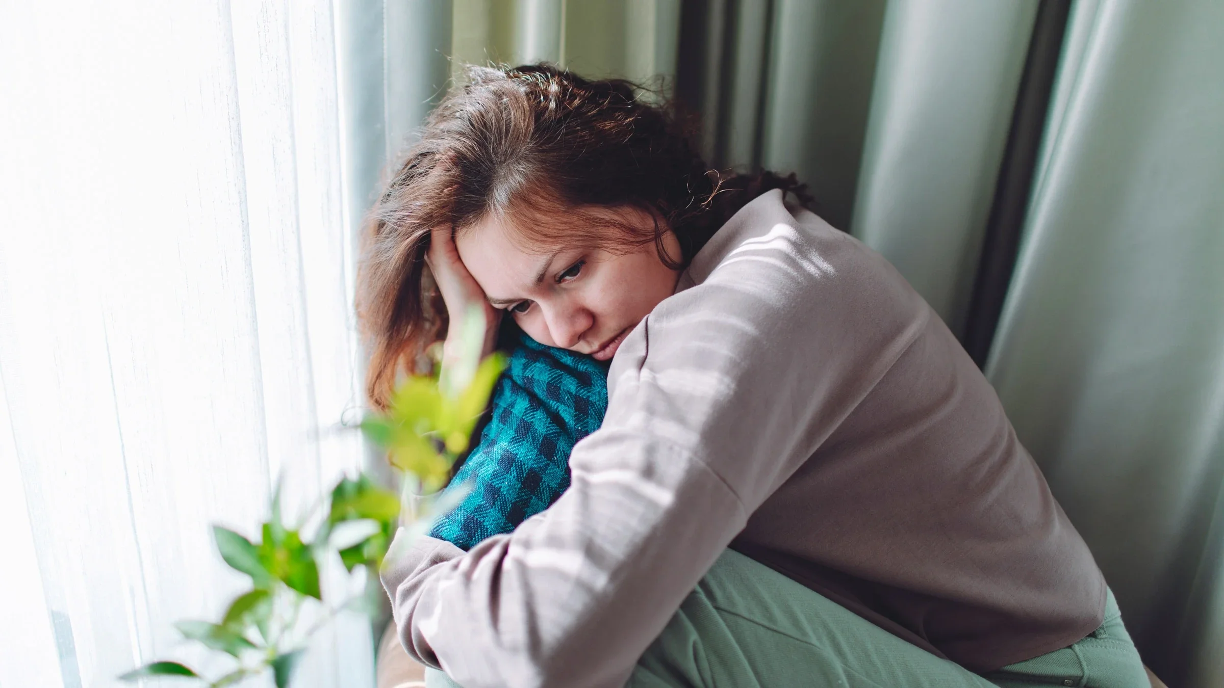 A woman sitting with her knees pulled into her chest with a sad and despondent look on her face.