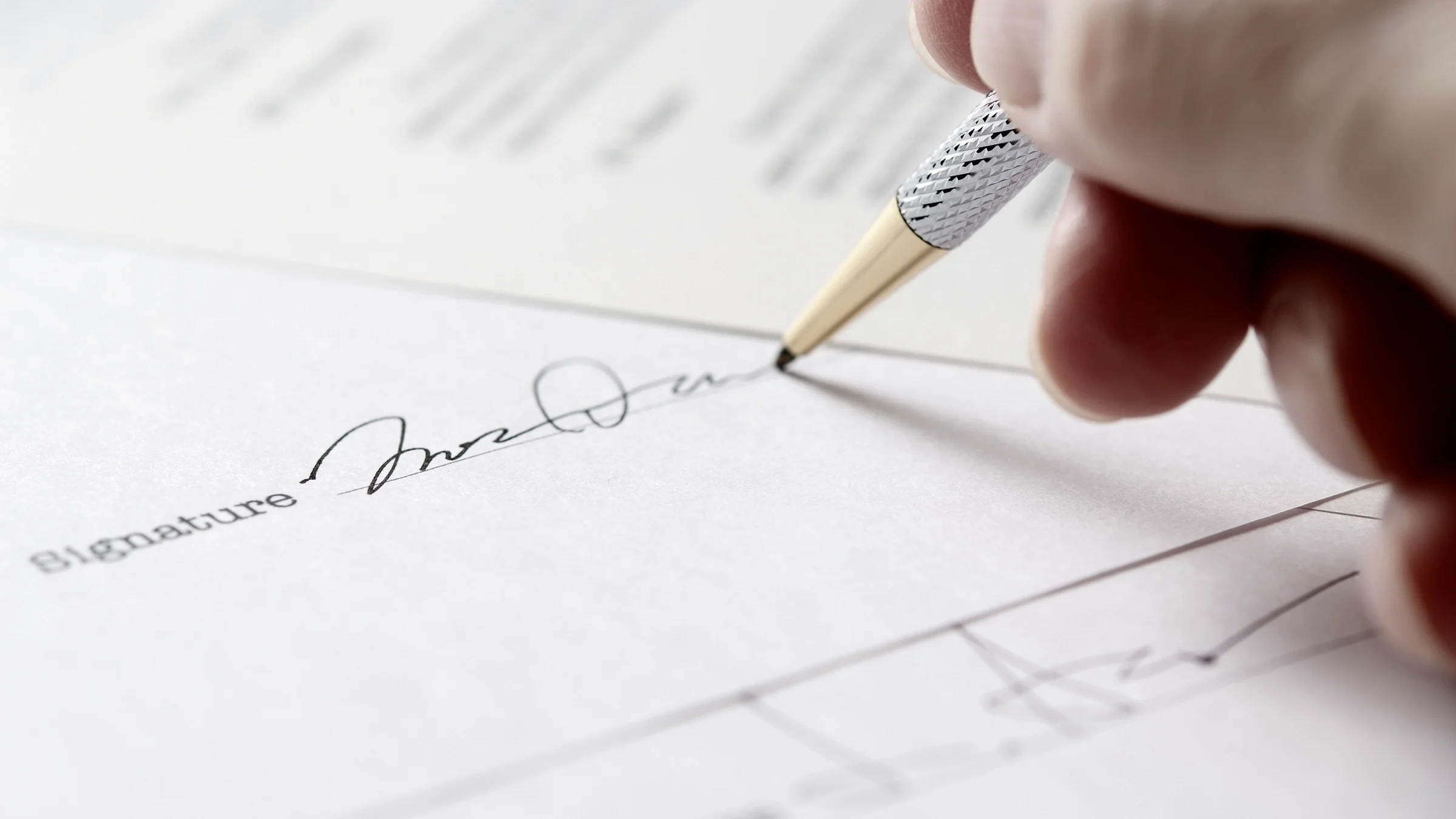 Close-up on a person signing their signature on a letter.