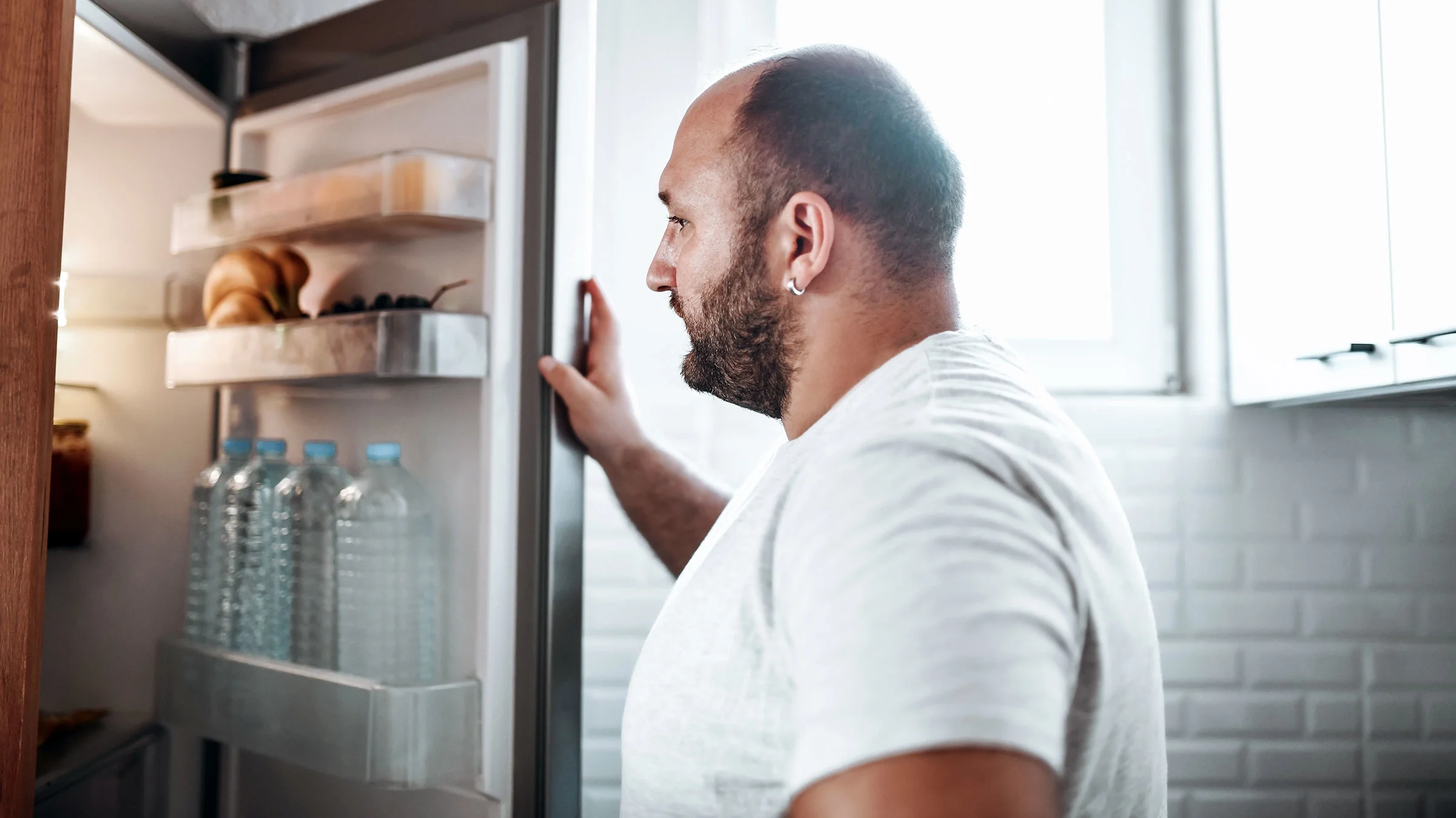 A man looks inside his open refrigerator. 
