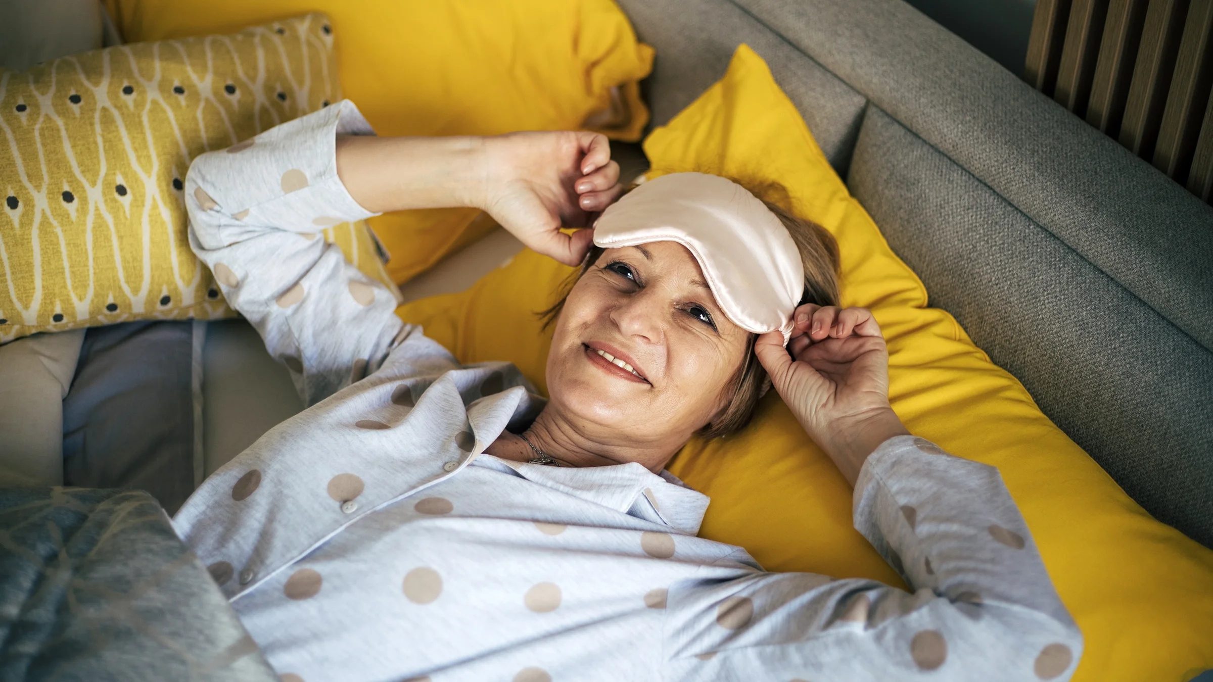 A woman removes her eye mask in bed after a good night’s rest.