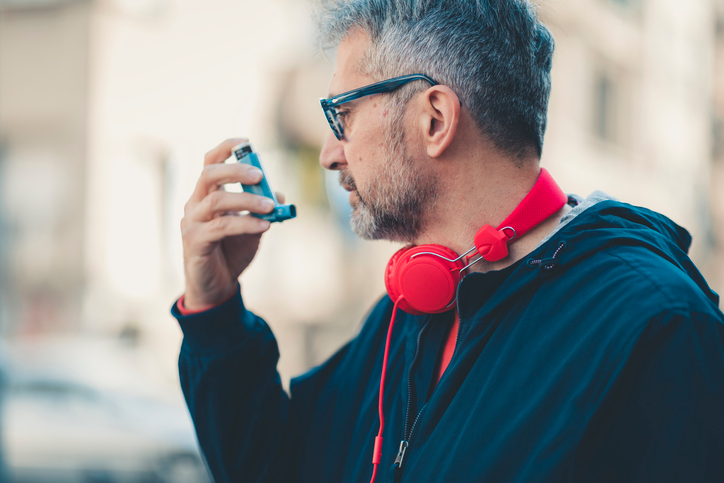 Close-up of a man outdoors bright red headphones around his neck while using an inhaler.