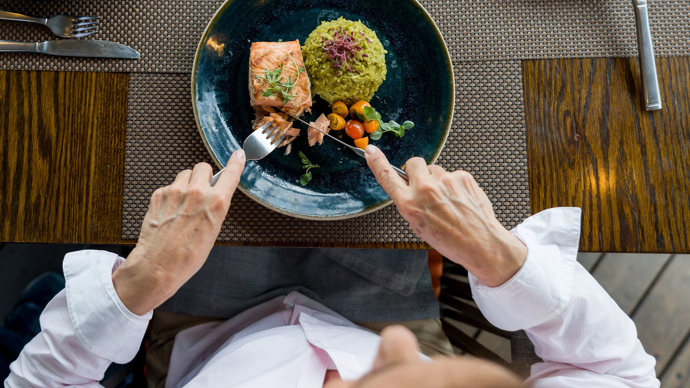 A woman cuts a piece of salmon for dinner at a restaurant.