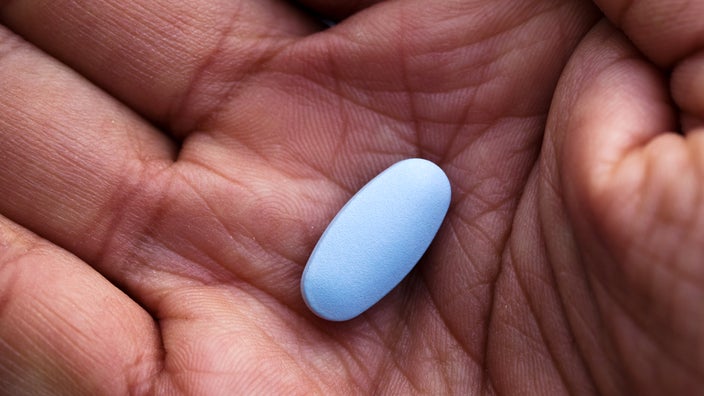 A man holds a blue pill in the palm of his hand.
