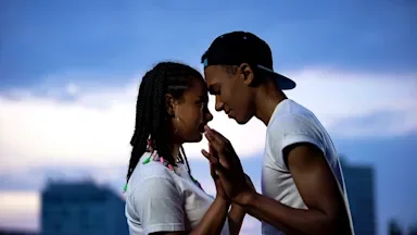 Couple standing with their foreheads touching and hands palm to palm outside on a dark cloudy day.
Motortion/iStock via Getty Images