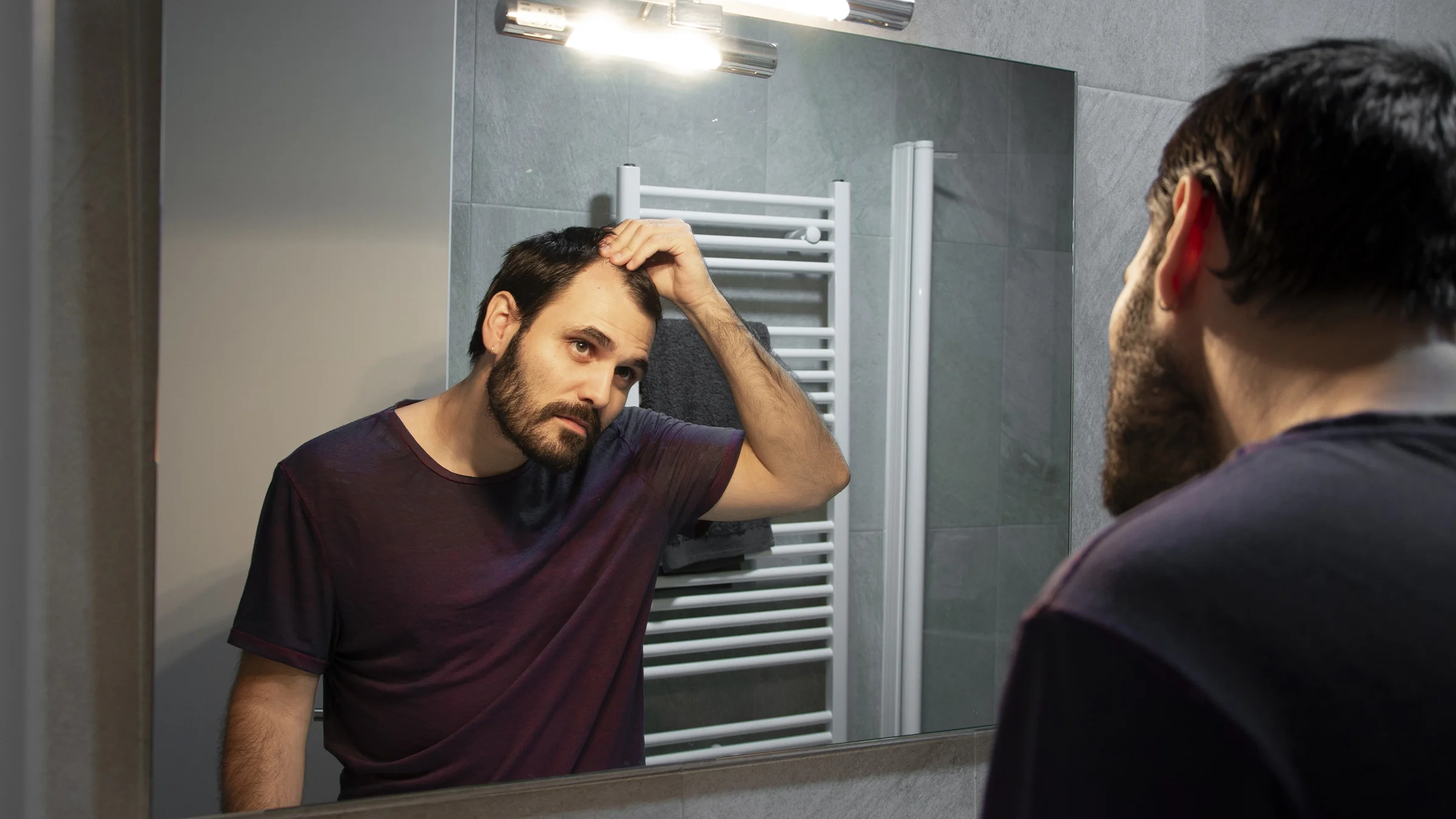 A man examines the reflection of his receding hairline in the mirror.