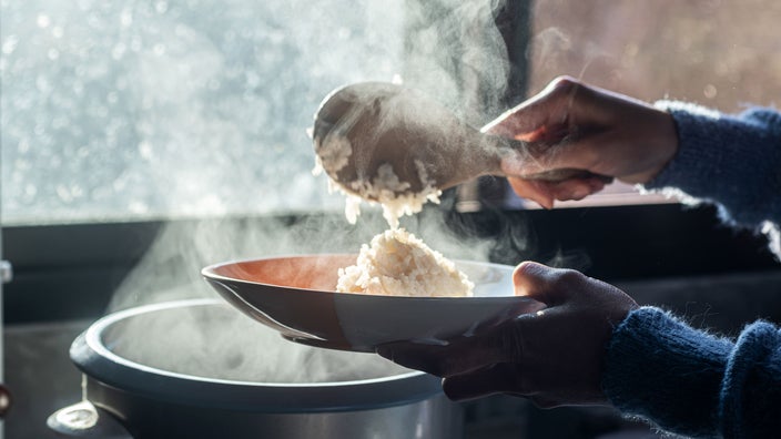 A close-up of a woman’s hands scooping rice onto a plate.