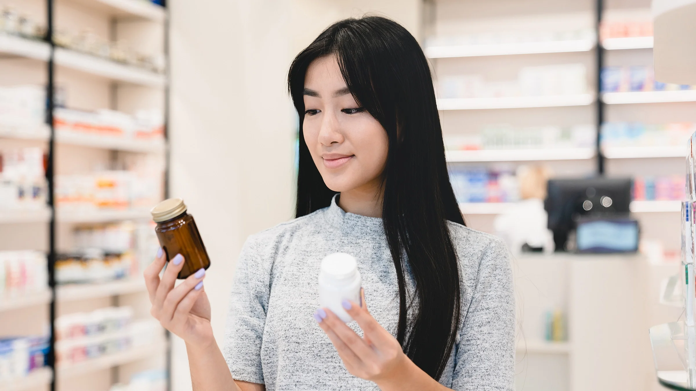 A woman is shown comparing two products in a pharmacy drugstore.