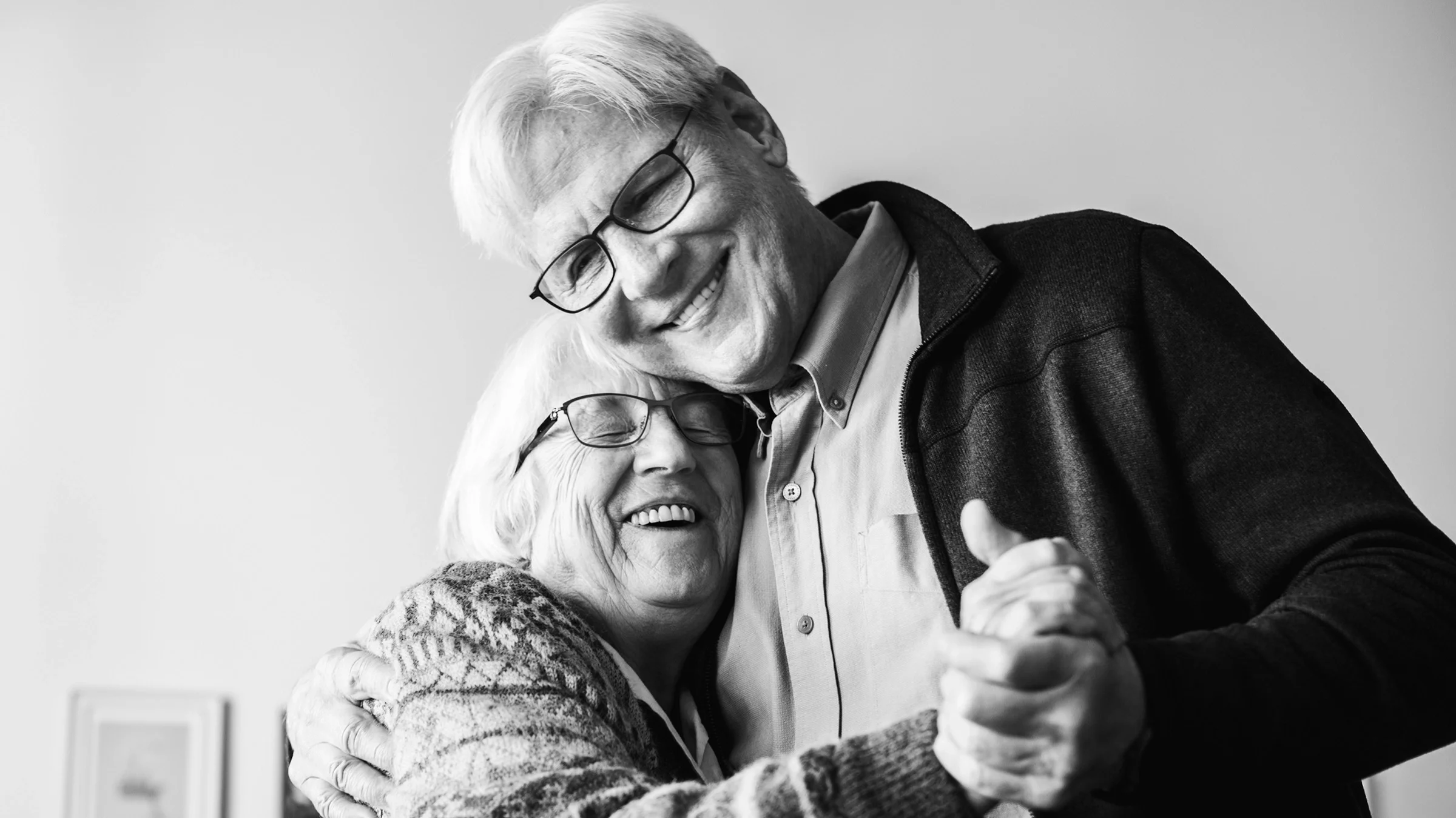 Black and white portrait of an elderly couple dancing in their living room.