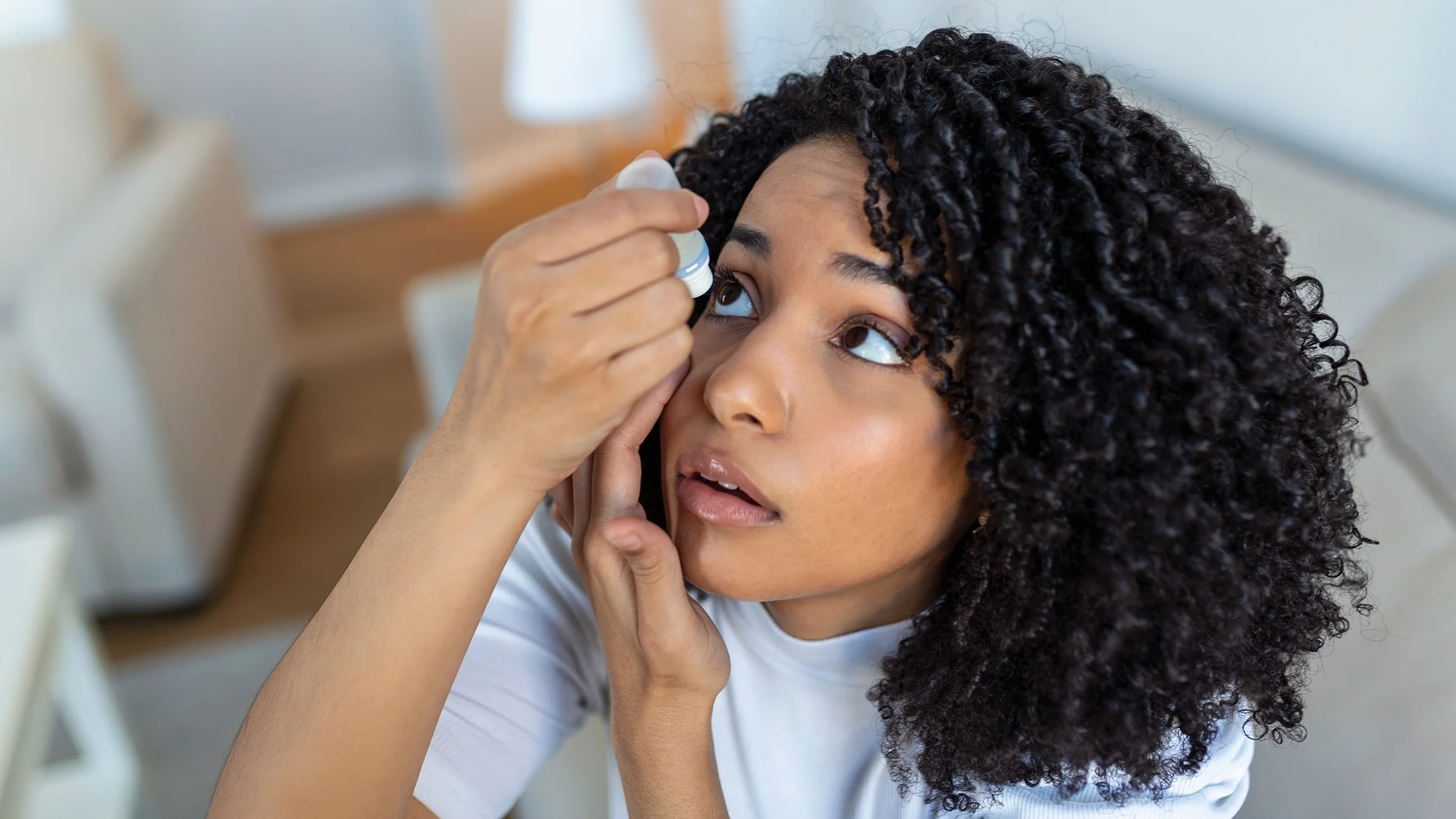 Young woman putting in eye drops as she tilts her head back.