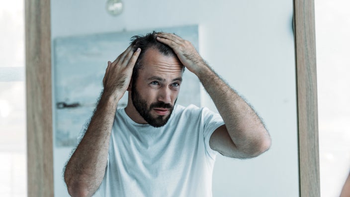 A man examines his receding hairline in the mirror.