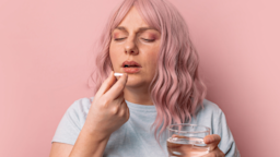 A sick person with pink hair taking a pill, against a pink background.
Irina Shatilova/iStock via Getty Images 