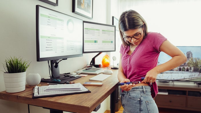 Young woman doing her insulin injection as she stands at her standing desk at home.