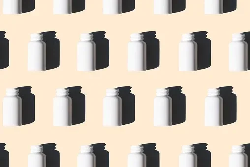 A pattern of white pill bottles on a tan or cream background with shadows falling on the background.
schlosann/iStock via Getty Images