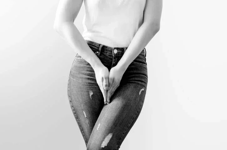 Black and white image of a woman's knees to chest as she is crossing her legs with her hands in front of her crotch.
todaydesign/iStock via Getty Images