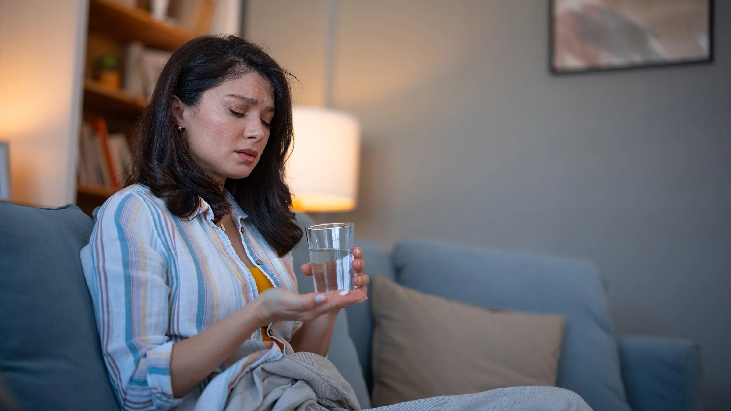 An anxious woman taking a pill with water at home.