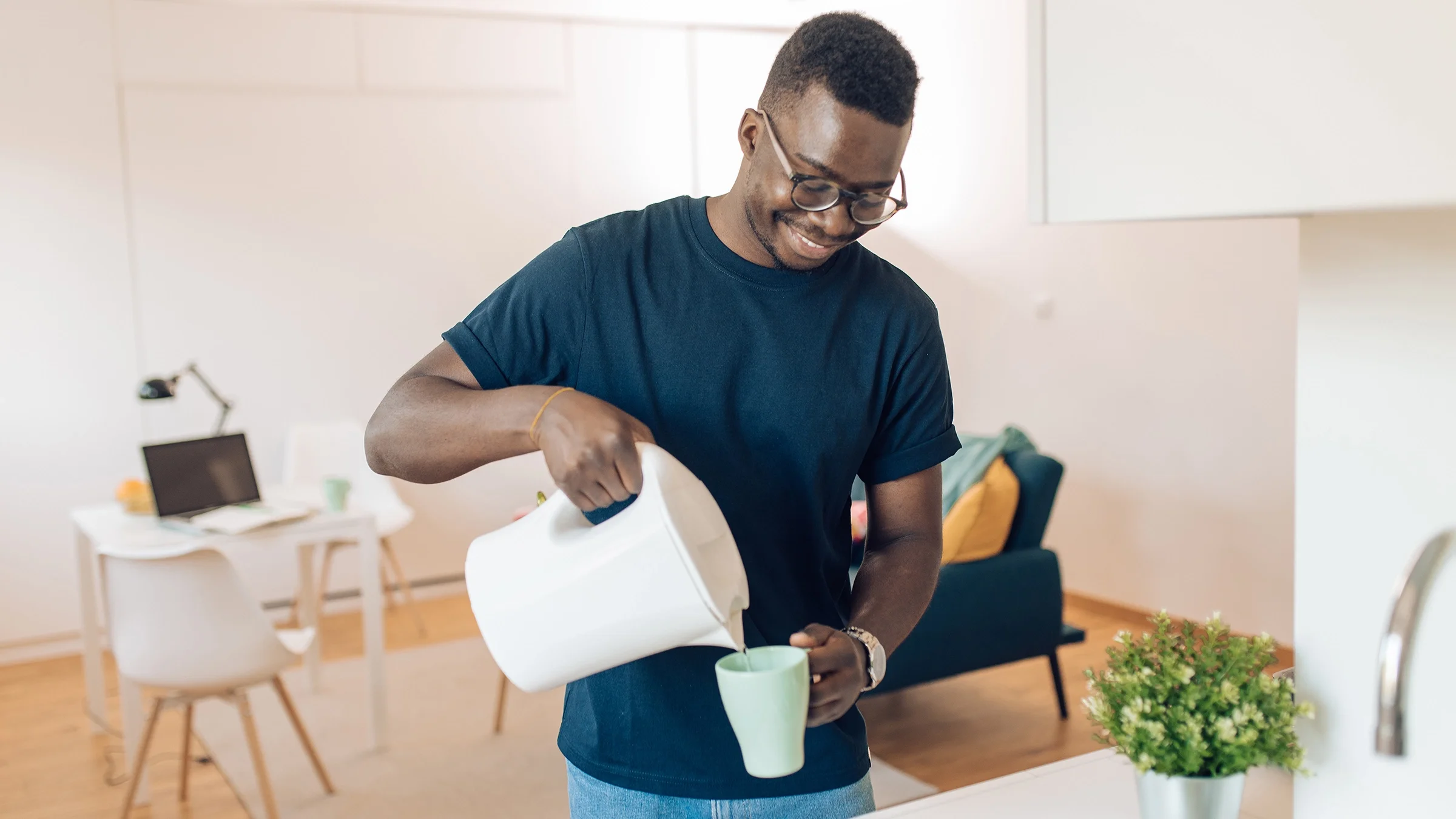 A man pours hot water from an electric kettle into a mug.