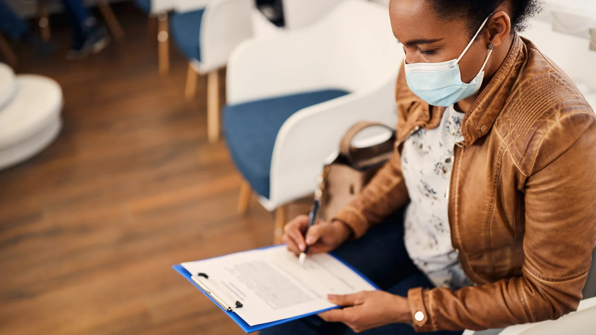 Woman filling out forms in hospital lobby. She is wearing a blue medical face mask.
Drazen Zigic/iStock via Getty Images
