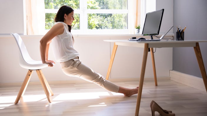 Woman does stretch exercise at office desk.