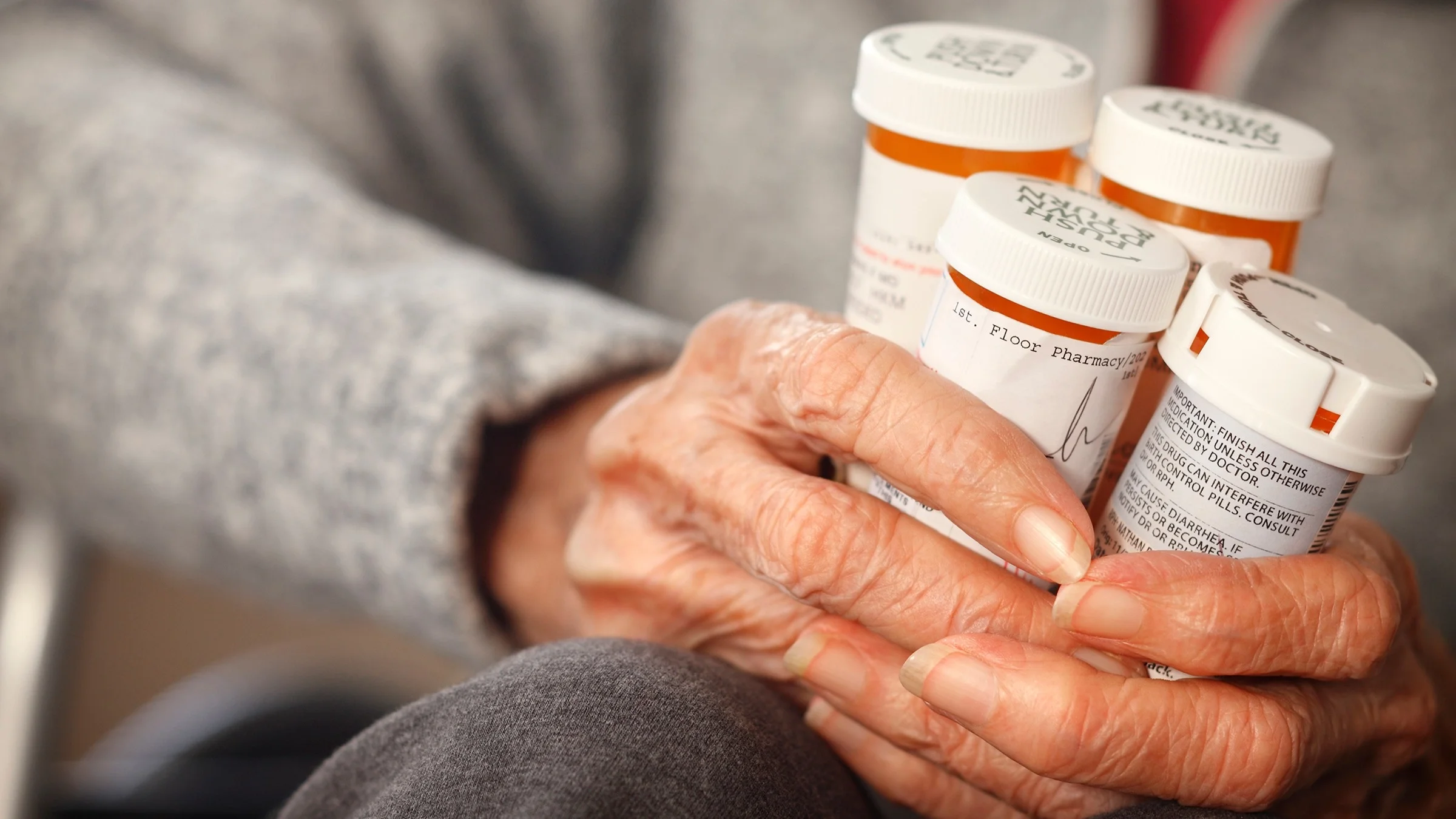 Close-up of an elderly person holding four prescription pill bottles in her hands.