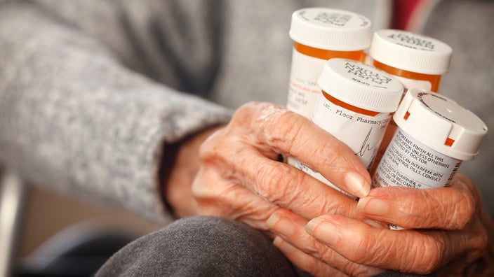 Close-up of an elderly person holding four prescription pill bottles in her hands.