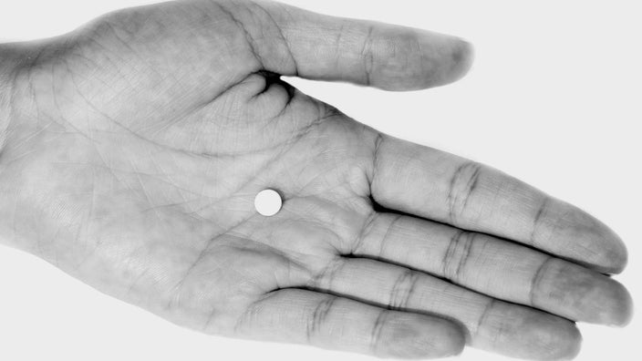 Black and white close-up of a person's palm with a tiny white round pill.