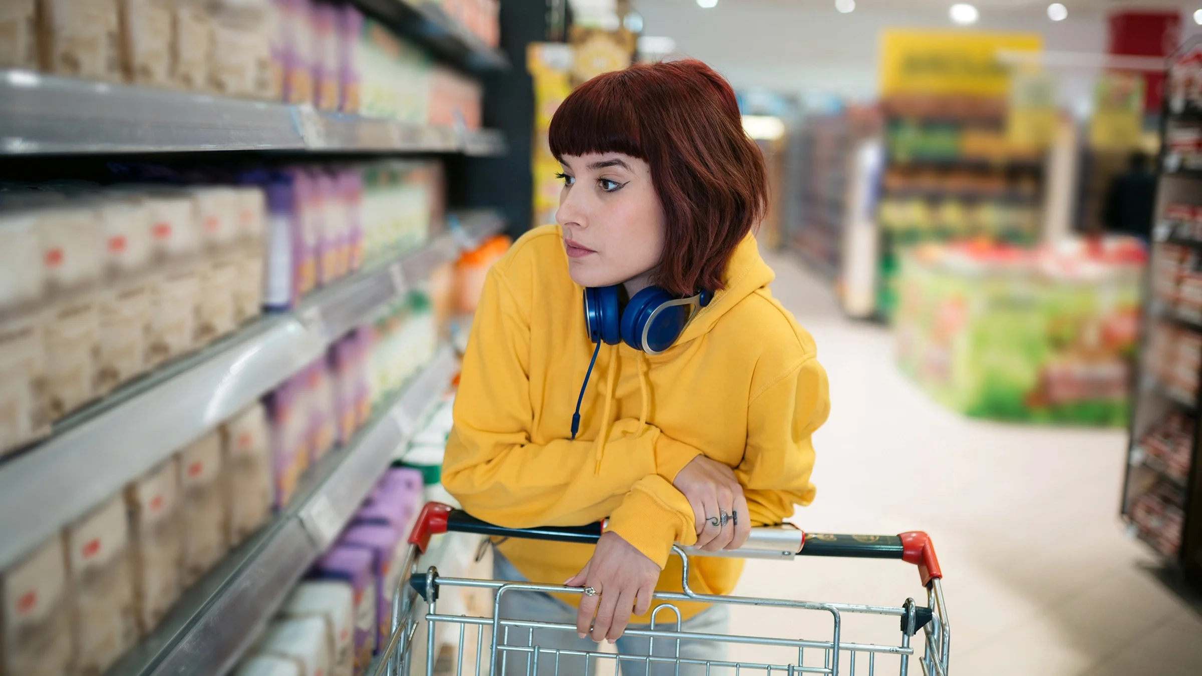 Woman pushing a shopping cart and looking at shelves of a supermarket.