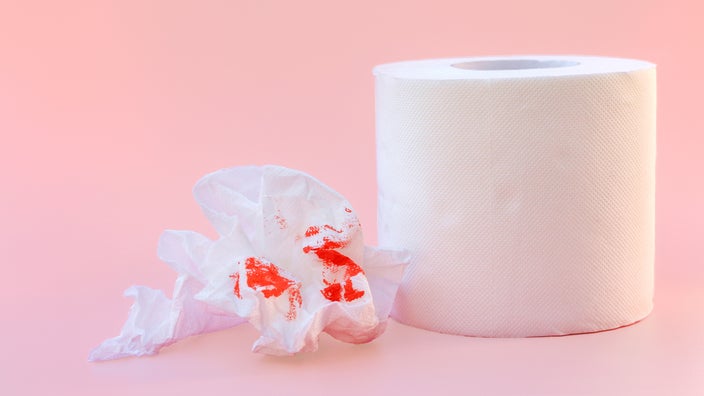 There’s a toilet paper roll with a crumpled bit next to it with red dye implying blood. The background is light pink.