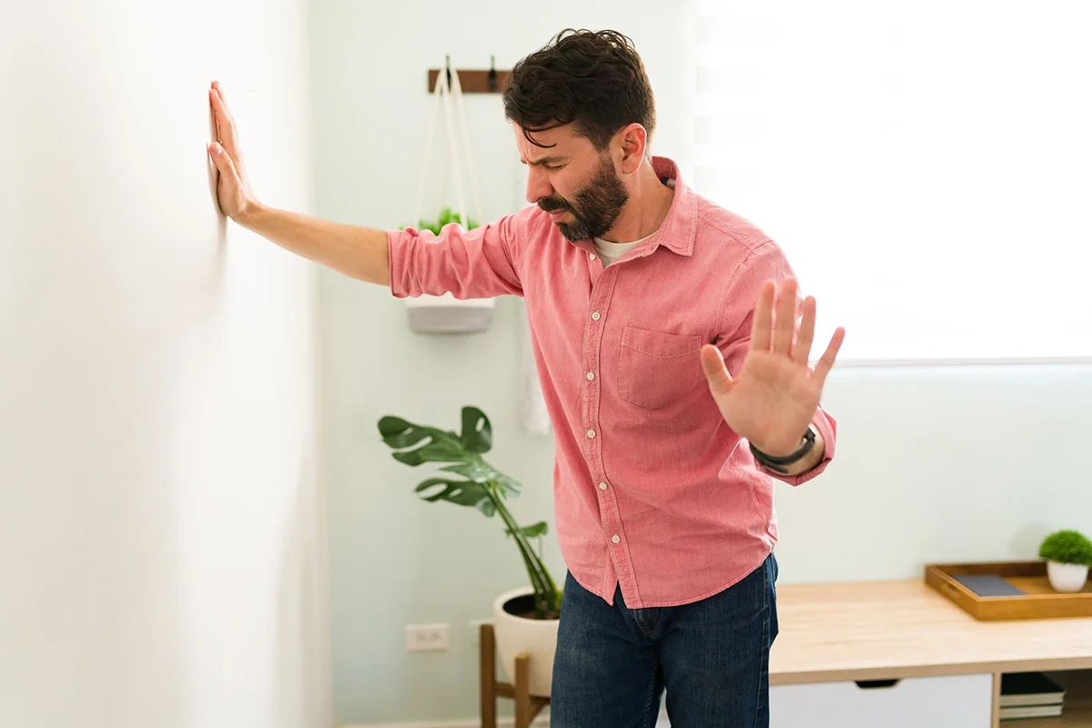Middle aged man experiencing some type of panic at home using the wall to brace himself with one hand.