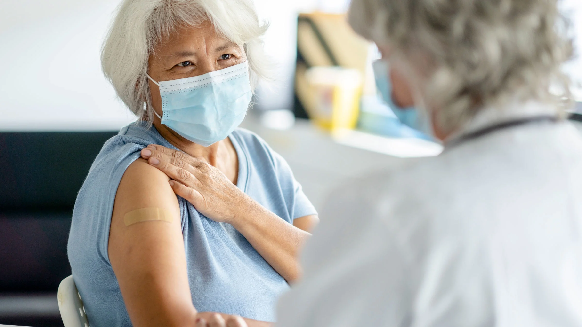 Older woman wearing a mask receives a vaccine.